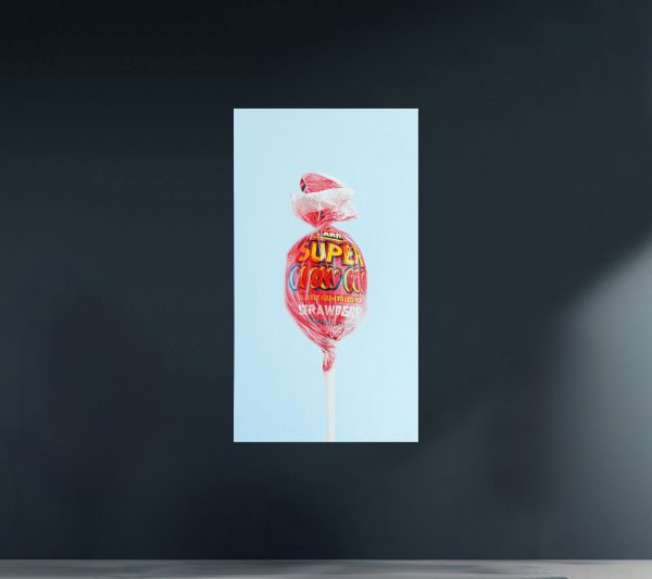 Super Blow Pop by Alexander Sheversky – 72x40 inch hyperrealist oil painting of a wrapped strawberry lollipop against a pale blue background.